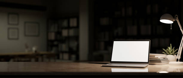 istock Workspace with laptop mockup, light from table lamp and copy space over blurred dark living room 1439948044