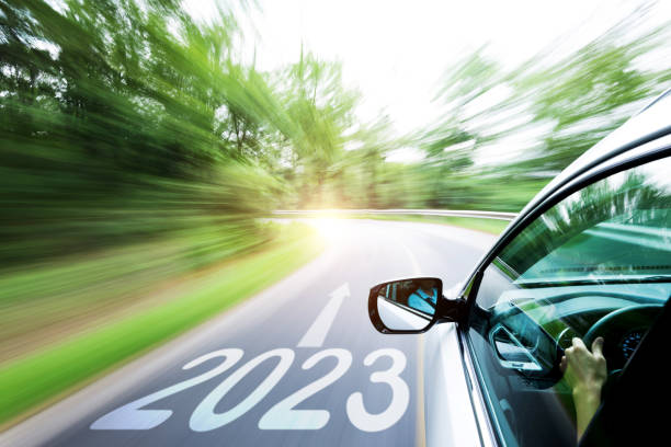 l'uomo guida l'auto attraverso la foresta, con il numero 2023 sulla strada - speed road sign sign forecasting foto e immagini stock