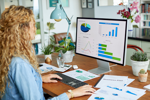 Businesswoman working on desktop PC at home office. Female professional is planning strategy on computer. She is reviewing 
financial charts.