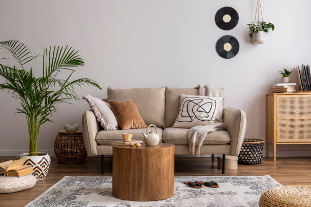 istock Creative composition of living room interior with beige sofa, carpet, pillow, plaid, coffee table and personal accessories. Beige wall. Home decor. Template. 1439953079