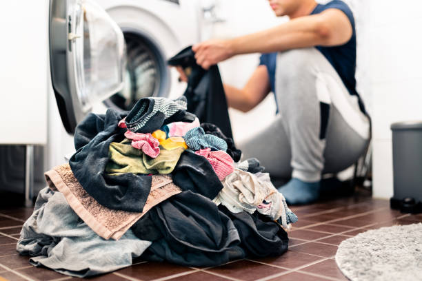 Laundry, washing clothes. Man loading washer machine and sorting by color and fabric.  Male homemaker doing house chores. Domestic work in family. stock photo