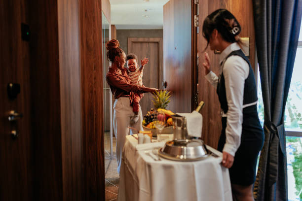 Room service delivery for hotel guests. A young waitress is delivering room service to some hotel guests. They are at the apartment door with their child waiving at the hotel staff. room service stock pictures, royalty-free photos & images
