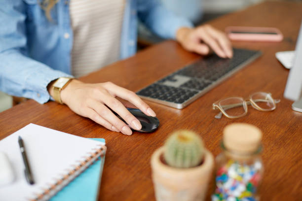 Hands of female entrepreneur using wireless keyboard and mouse on table. Businesswoman is working in home office. She is telecommuting.