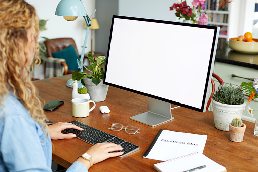 Female entrepreneur using desktop PC on table while working at home office. Businesswoman is looking at blank screen of computer. She is typing on keyboard.