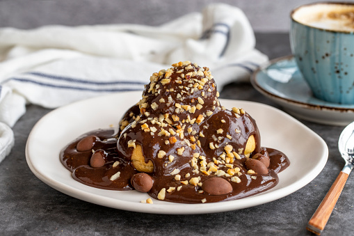 Profiterole dessert on dark background. Traditional french cuisine delicacies. Profiterole dessert topped with chocolate and hazelnut pieces. close up