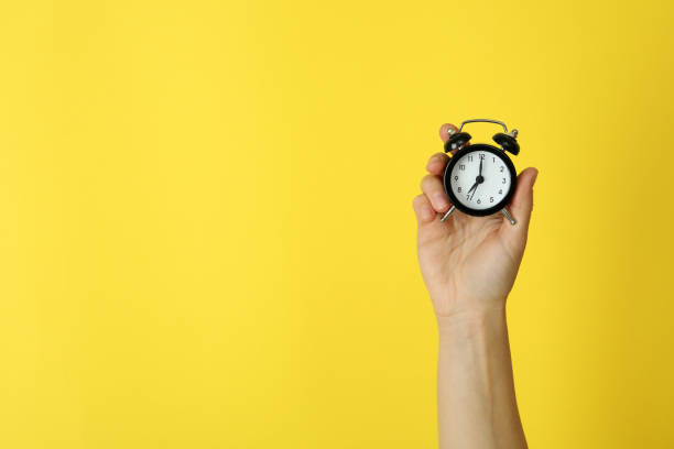 istock Female hand holds alarm clock on yellow background 1439960785