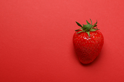 Single fresh tasty strawberry on red background