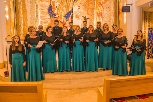 A large group of choir singers stand side by side in the cathedral rehearsing before a classical music concert