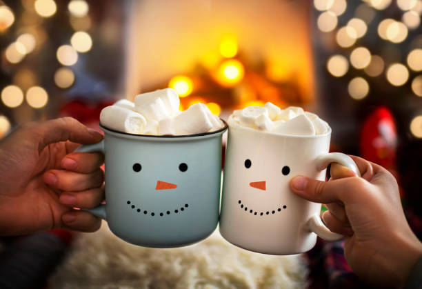 mom and child are relaxing together on a cozy winter evening by the fireplace, close-up of two hands with snowman face cup of hot cocoa with marshmallows. christmas holidays, happy moments at home. - vinter bildbanksfoton och bilder