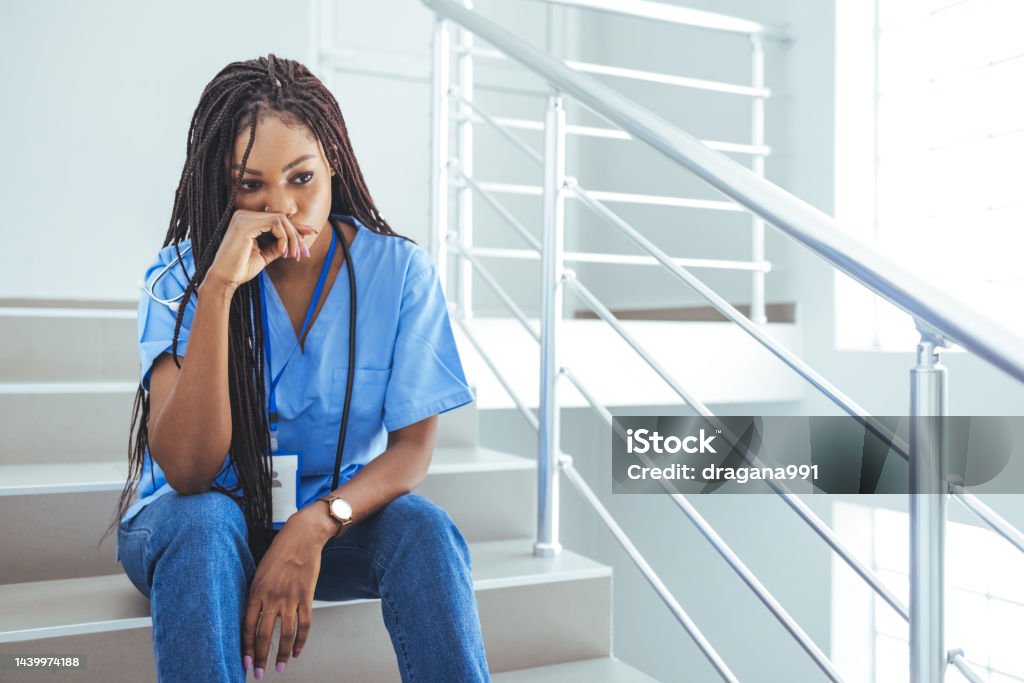 Close up of upset female nurse. Shot of a young nurse looking stressed out while sitting at a window in a hospital. Mentally and physically exhausted. Close up of upset female nurse. Worried and stressed doctor sitting on corridor Nurse Stock Photo