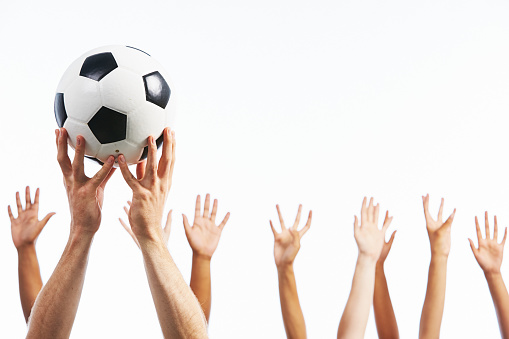 Many hands being held up with a soccer ball being held high in the air.