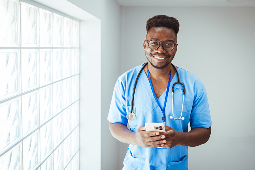 Medical professional working in a hospital. He is dressed in scrubs looking at the camera smiling with a stethoscope around his neck. Happy in his Profession. Male nurse with stethoscope standing at clinic.