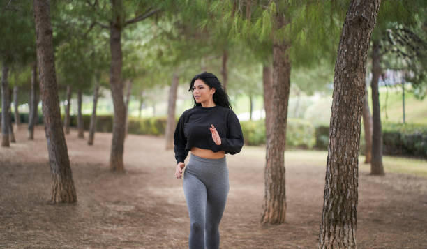an athletic woman running in a park through pine trees stock photo