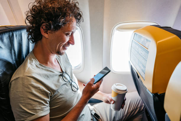 istock Young Man Using Smart Phone And Drinking Coffee In An Airplane 1439979349