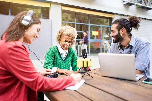 istock Young woman interviewing a man in a casual radio studio outdoors. Millennial people using technology, computers, headphones, microphone... 1439979404