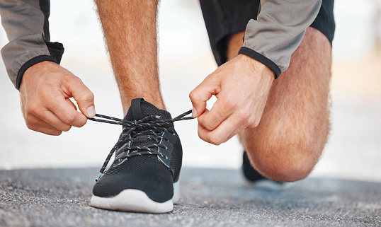Closeup shot of a young male athlete tying his shoelaces before going on a run outside. Sporty man fastening his running footwear is fastened before a jog outside. Increase your endurance with cardio