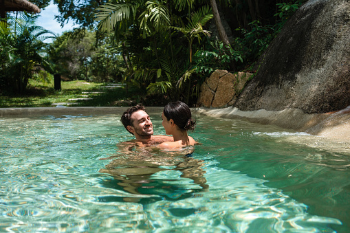 Smiling couple enjoying the cold pool surrounded by rocks after sauna on their vacation in a luxury villa.
