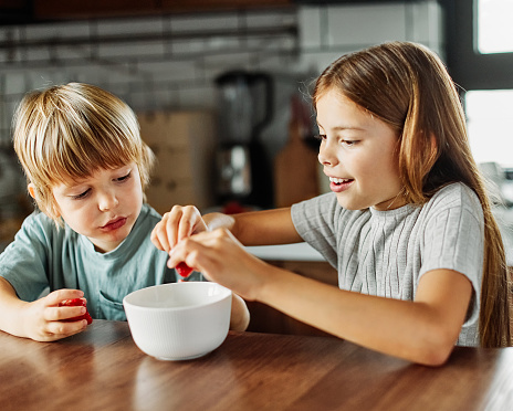 Portrait of brother and sister having fun together eating breakfast strawberries in kitchen