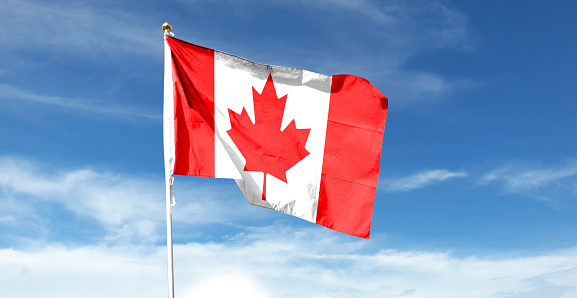 Close up of Canadian flag at half mast blowing freely from the flag pole on windy sunny day.