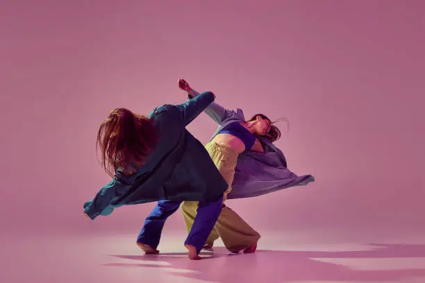 Contemporary dance couple in motion and action isolated on crystal pink background. Young stylish fashionable girls dancing. Concept of modern art, fashion, youth style and creativity
