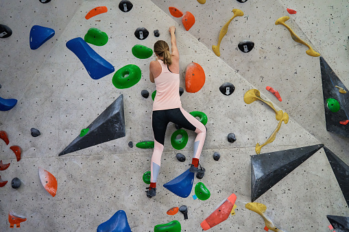 Side view of Caucasian athlete scaling boulder wall free of rope and harness, with padded mats below, to help build strength and improve climbing technique.