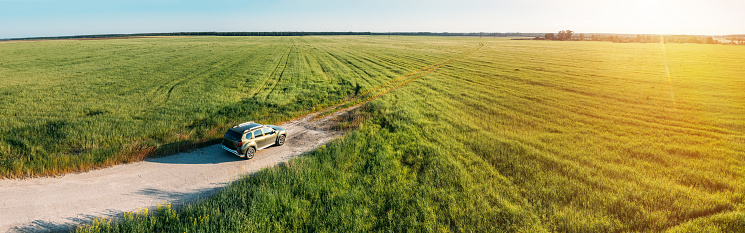 Aerial view of car SUV parked near countryside road in field rural landscape. Aerial view of car SUV parked near countryside road on a sunny summer evening. Panorama, panoramic view.
