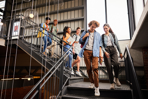 Diverse group of smiling young college students talking together while walking down stairs at school between classes