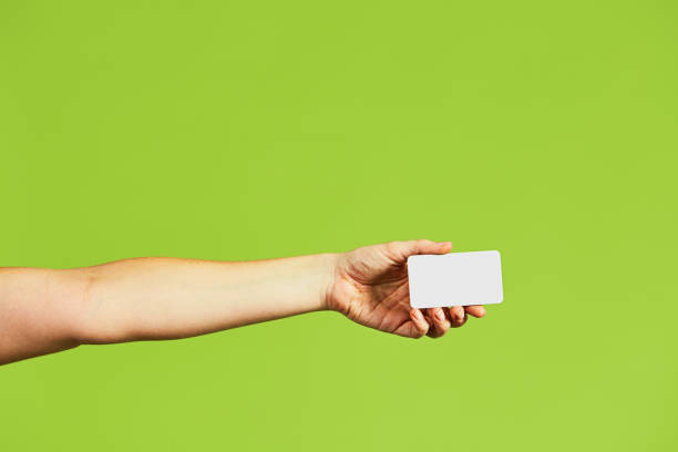 istock Woman with arm extended holds a blank card, with copy space, on a green background 1440001850