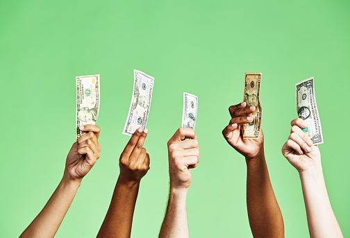 Diverse group of hands holding up US dollar banknotes of various denominations on green background