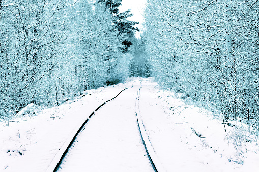 Single-track railway in the forest on which carry logs, unevenly laid rails. Snowfall covered the road