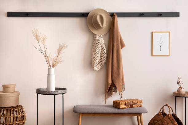 Creative composition of warm and cozy entryway interior with mock up poster frame, gray bench, coddee table, white vase with dried flowers, hanger, brown scarf, hat, round box, braided basket and personal accessories. Home decor. template. composición creativa del interior de entrada cálido y acogedor con marco de póster de maqueta, banco gris, mesa de coddee, jarrón blanco con flores secas, percha, bufanda marrón, sombrero, caja redonda, cesta trenzada y accesorios personales. decoraci