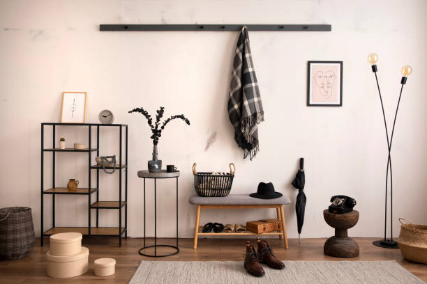 istock Interior design if entryway interior with mock up poster frame, wooden gray bench, simple black rack, beige box, hanger, wooden coffee table, gray rug, plaid and personal accessories. Home decor. Template. 1440004219