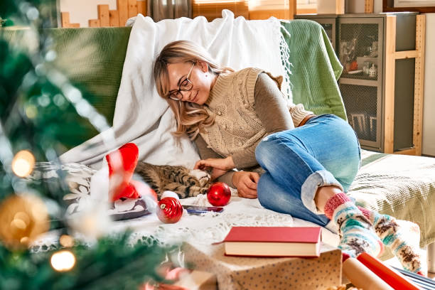 istock Cheerful blonde woman in festive mood hugging sleeping tabby cat  on couch while preparing for celebration Christmas or New Year. Winter holiday concept. 1440007684