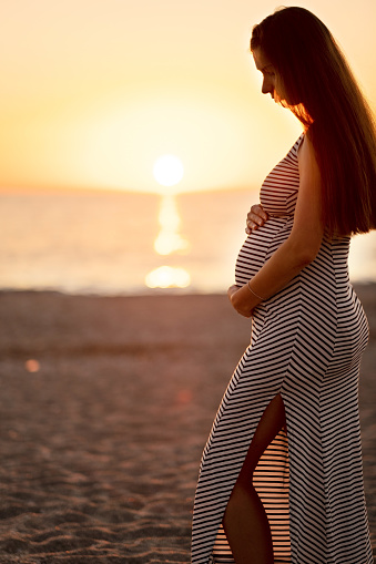 Pregnant woman at beach on background of sea at sunset in evening.Female silhouette, mother.Happy maternity and travel, motherhood concept.Copyspace.