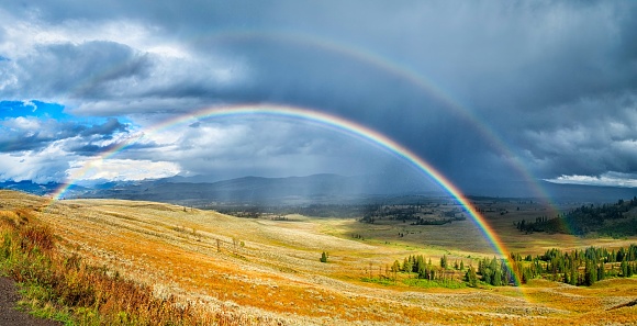 A rainbow over a beautiful  green and yellow field under the cloudy sky