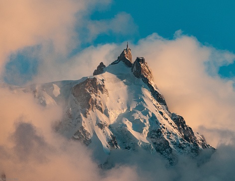 A picture of Aiguille du Midi covered in the snow and the fog under a blue sky in the French Alps