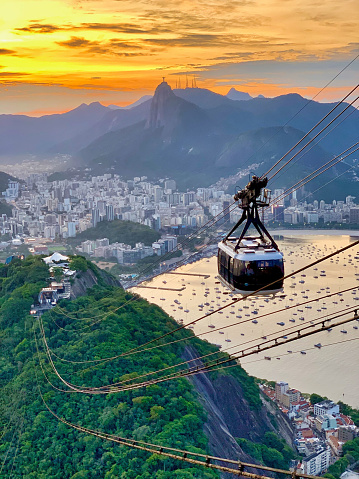 Sugarloaf mountain cable car during sunset in Rio de Janeiro, with Christ the Redeemer statue and boats in the background.