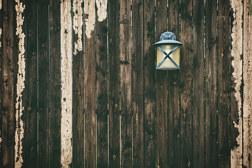 A closeup shot of a black metal sconce lamp on an old wooden fence