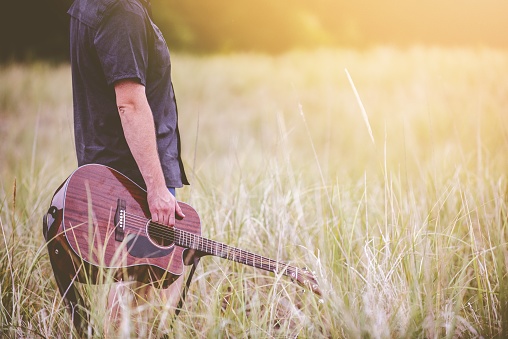 A beautiful shot of a male walking in a wild field and holding a guitar in his hands