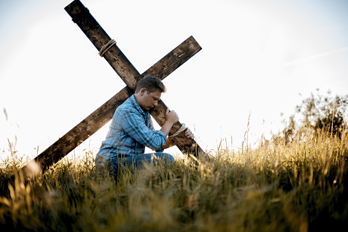 A shallow focus shot of a male carrying a handmade cross