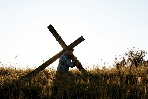 A male carrying a hand made a wooden cross through the dry grassy field