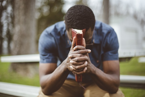 A young African-American male sitting with closed eyes with the Bible in his hands