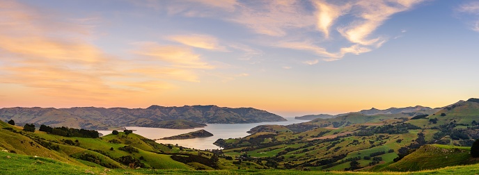 A panoramic shot of a green meadow in front of a lake, Akaroa, Banks Peninsula, New Zealand