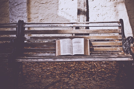 A closeup shot of an open bible on a wooden bench with a blurred background