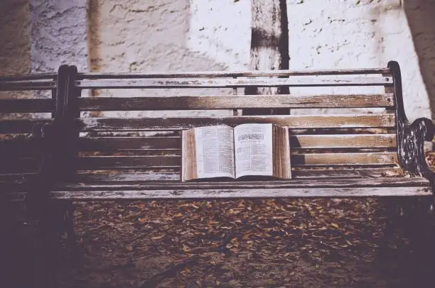 Photo of Closeup shot of an open bible on a wooden bench with a blurred background