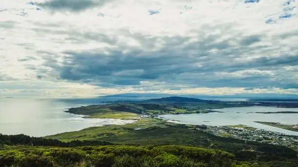 Photo of Panoramic view of a green forest against the sea in Invercargill, New Zealand on a cloudy day