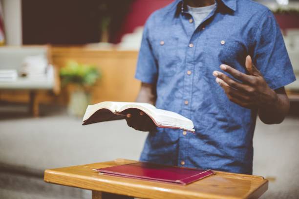 primo piano di un maschio che legge la bibbia vicino a un supporto di legno con uno sfondo sfocato - preacher foto e immagini stock