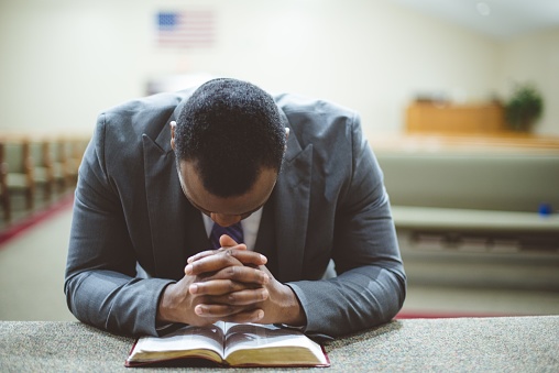 A lonely african-american male praying with his hands on the Bible with his head down
