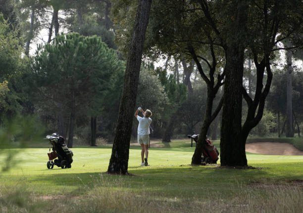 femme qui vient de frapper la balle de golf, parmi les arbres ombragés. - golf cart golf mode of transport transportation photos et images de collection