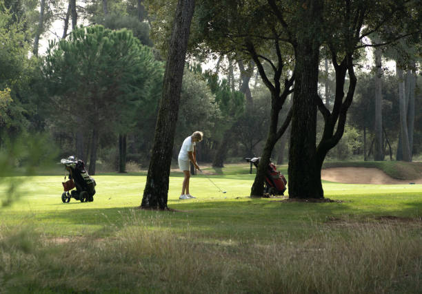 femme sur le point de frapper la balle de golf parmi les arbres ombragés. - golf cart golf mode of transport transportation photos et images de collection